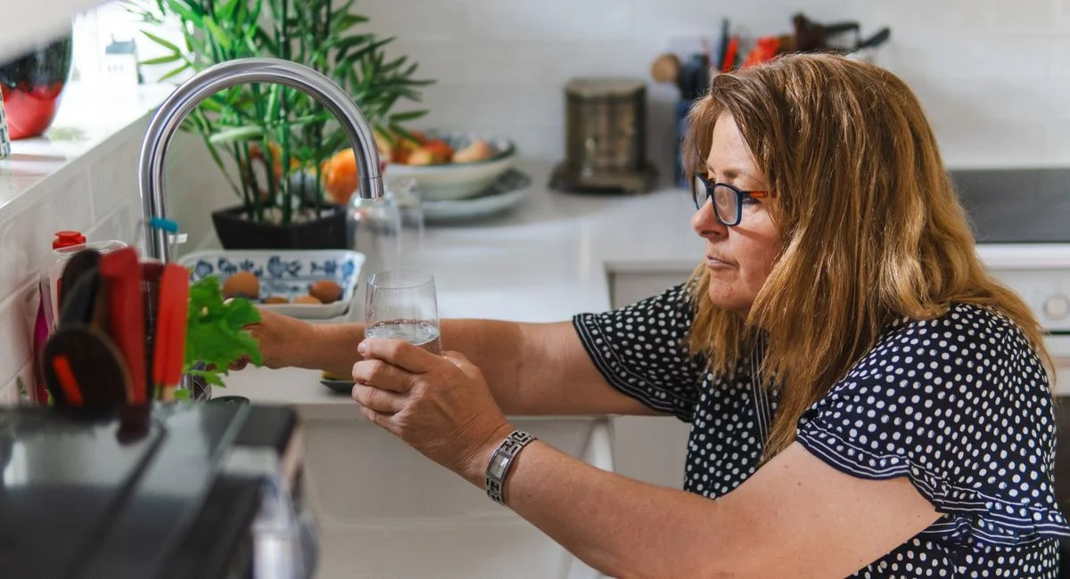 A middle-aged woman filling a glass with water in a modern kitchen setting.