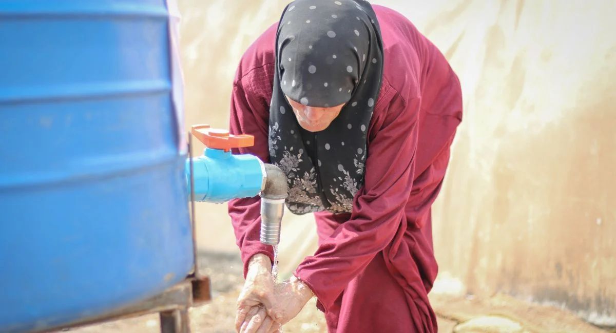 Middle Eastern woman washing hands at an outdoor water tap in Idlib, Syria.