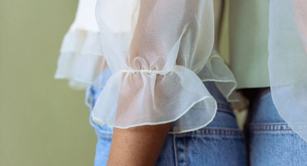 Close-up of a sheer white blouse with ruffles paired with denim jeans, showcasing modern fashion.