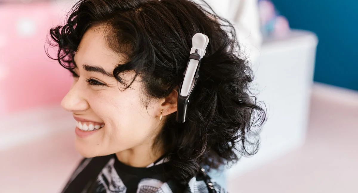 Side profile of a woman with curly hair smiling in a hair salon with a hair clip.