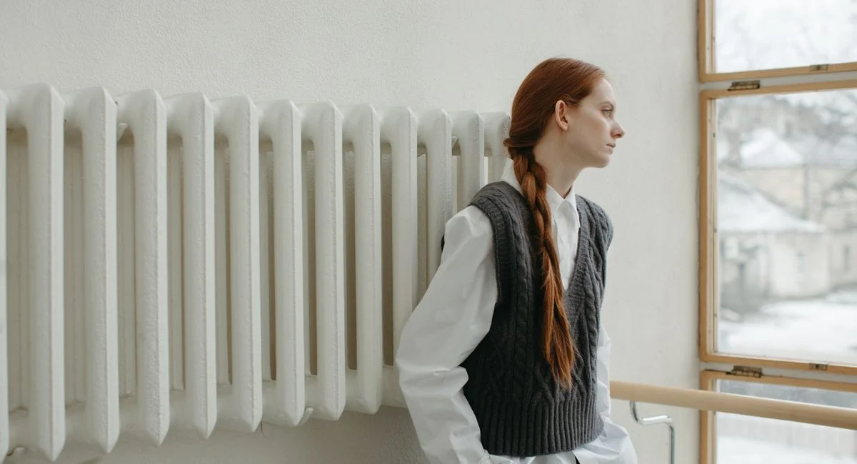 A contemplative redhead woman in a sweater vest gazing out of a window, capturing a serene indoor moment.