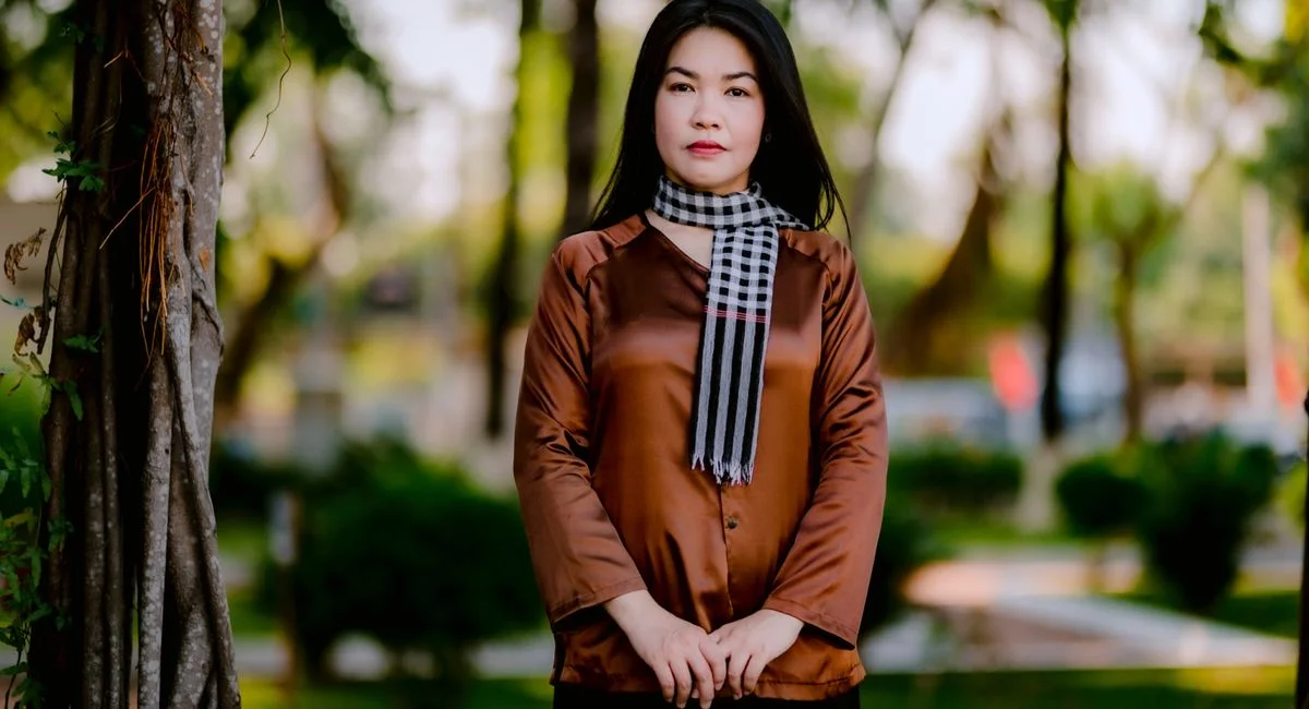 Confident woman in silk blouse and scarf posing gracefully outdoors in a green park.