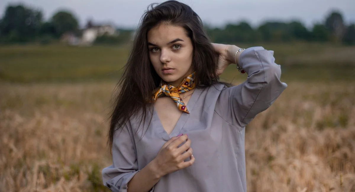 Elegant portrait of a young woman wearing a scarf in a rural field setting.