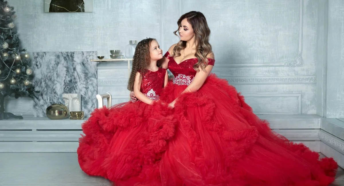 Mother and daughter in matching red gowns posing elegantly in a festive indoor setting.