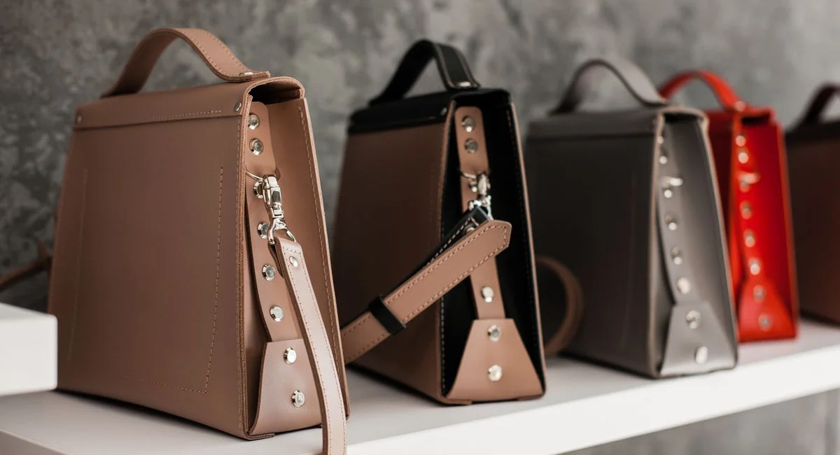 Luxury leather handbags displayed on a white shelf, showcasing minimalistic design and various colors.