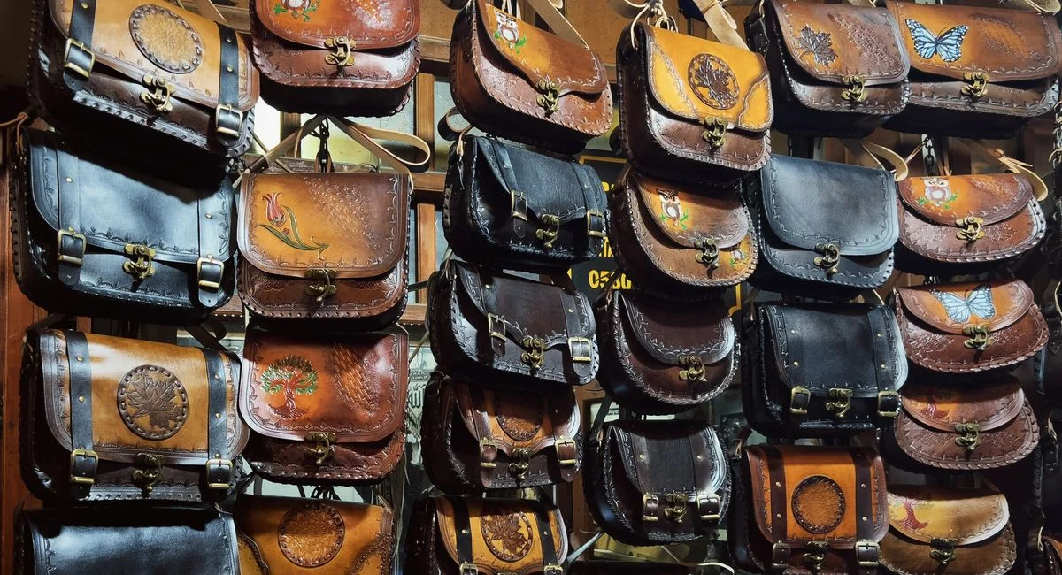 A collection of handcrafted leather bags with artistic designs on display at a shop.